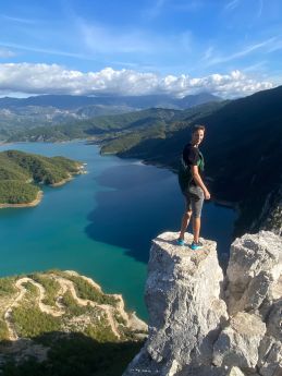 Jongen staat op een rotsrand hoog boven turquoise meer en kronkelende bergweg, berglandschap op de achtergrond
