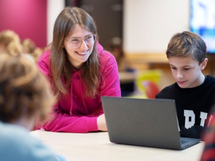 Leerling achter de laptop krijgt uitleg van een docent
