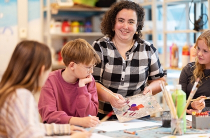 Docent staat aan de tafel bij drie leerlingen