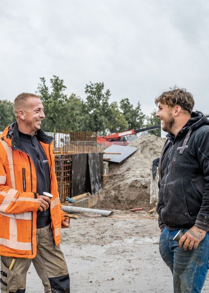 Twee bouwvakkers staan samen op de bouw een kopje koffie te drinken en te kletsen