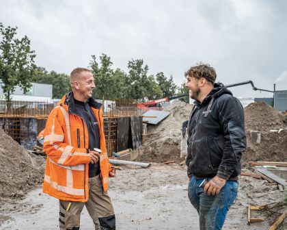 Twee bouwvakkers staan samen op de bouw een kopje koffie te drinken en te kletsen