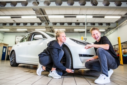 Jongen en meisje poseren lachend voor een auto in de werkplaats