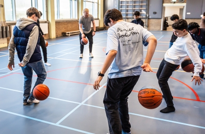 Leerlingen in een sportschool die een basketbal laten stuiteren