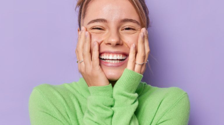portrait-happy-young-female-model-keeps-hands-cheeks-smiles-broadly-shows-white-teeth-feels-glad-expresses-sincere-emotions-wears-green-turtleneck-isolated-purple-studio-background 1 Blonde mevrouw