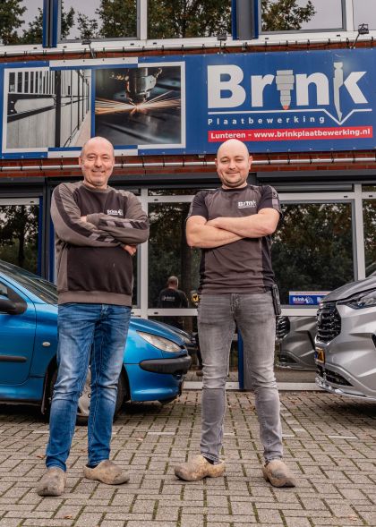 Twee mannen voor pand van bedrijf, achter hen staan twee auto's