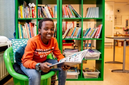Jongen zit met een tijdschrift in zijn hand voor een boekenkast