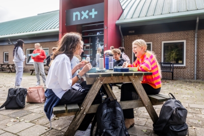 Een groep leerlingen zit aan een picknickbankje op het schoolplein van NXT Doorn.