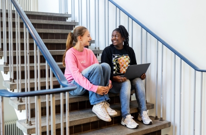 Twee leerlingen zitten met laptop op schoot op de trap.
