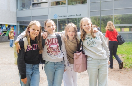 Decoratief beeld. Vier leerlingen poseren buiten voor het schoolgebouw.