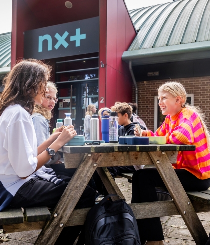 Leerlingen lunchen aan een picknicktafel buiten voor de school