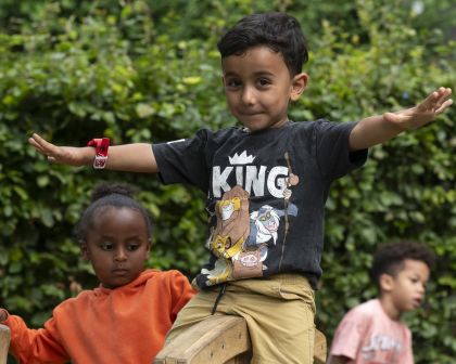 Vrolijk jongetje met Lion King t-shirt spreidt zijn armen op een klimtoestel.