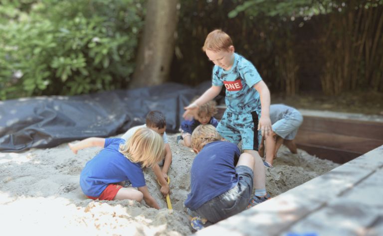 Kleuters spelen in een zandbak, ze graven een put.