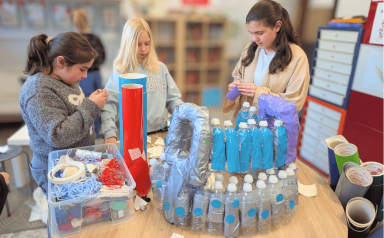 Drie kinderen werken samen aan een project met wegwerpmateriaal.