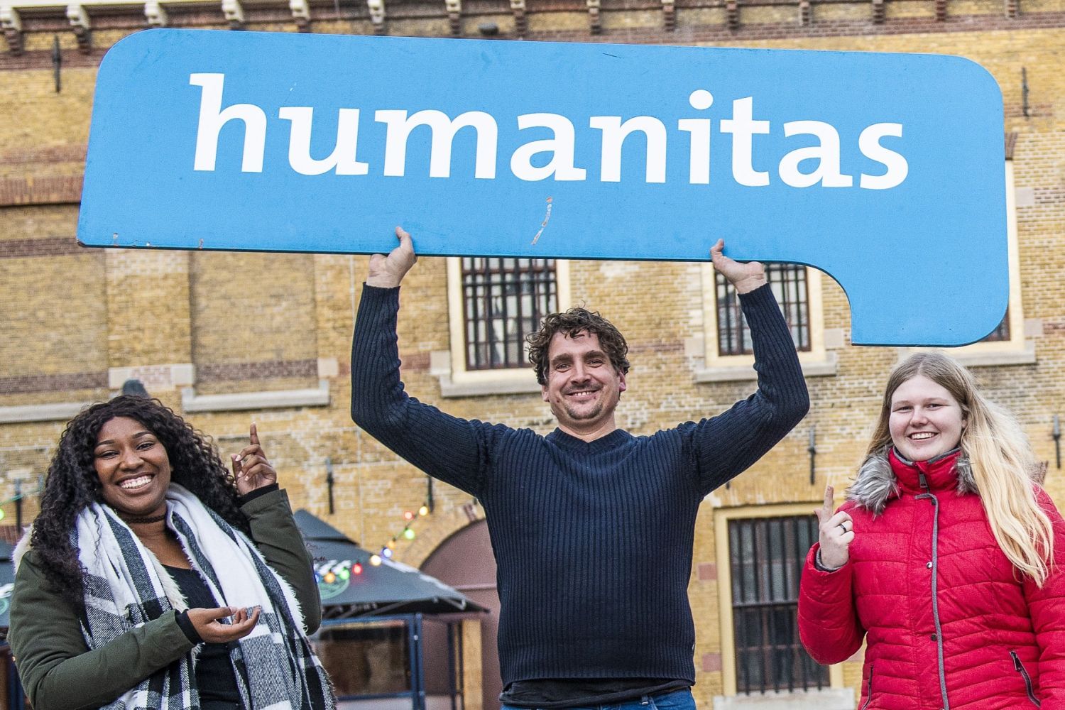 Enthousiaste vrijwilligers van humanitas houden bord omhoog met Humanitas erop