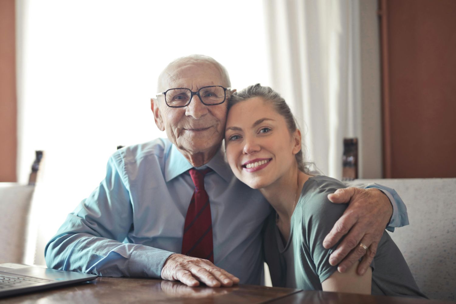 Jonge dame en oudere meneer zitten aan tafel en poseren voor een foto