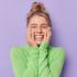 portrait-happy-young-female-model-keeps-hands-cheeks-smiles-broadly-shows-white-teeth-feels-glad-expresses-sincere-emotions-wears-green-turtleneck-isolated-purple-studio-background 1 Blonde mevrouw