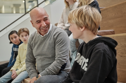 Foto van een docent en een aantal leerlingen op de trap van het gebouw van Academie Tien. Ze voeren een ontspannen gesprek en de docent lacht naar een van de leerlingen.