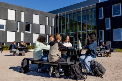 Leerlingen zitten aan picknicktafel op schoolplein met lunch