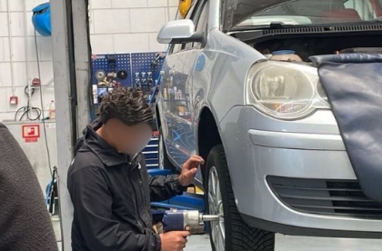 Een leerling vervangt een autoband in een vakgarage