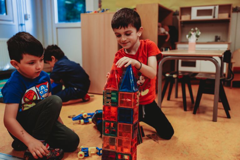 Two young boys using toy blocks to build a house together in class Two young boys using toy blocks to build a house together in class