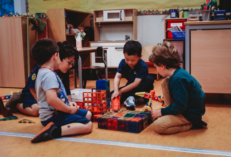 A group of 4 boys sits on the classroom floor around toy building materials A group of 4 boys sits on the classroom floor around toy building materials