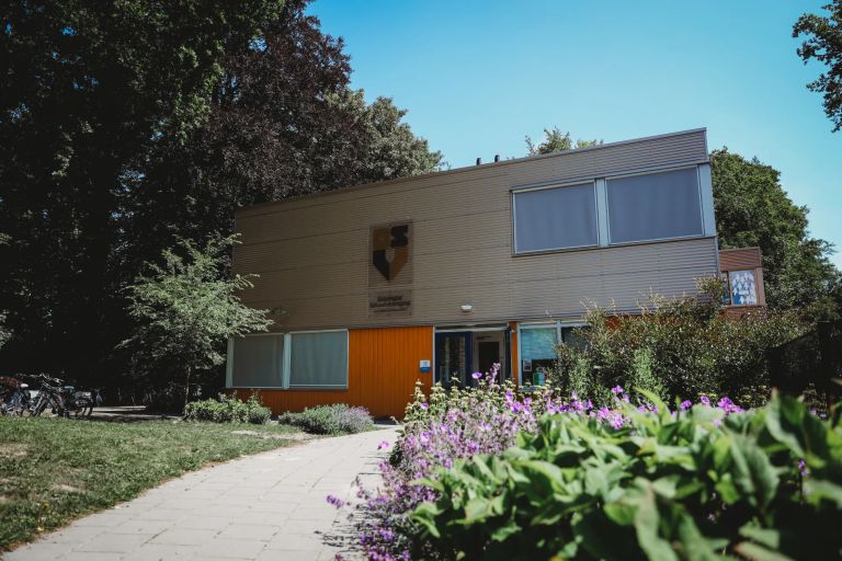 The International Primary School Groningen's school facade, with a paved path and blooming bushes The International Primary School Groningen's school facade, with a paved path and blooming bushes