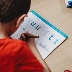 A boy leans over his worksheet, tracing out the English alphabet A boy leans over his worksheet, tracing out the English alphabet