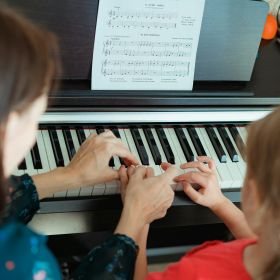 A music teacher and a young girl play piano together during a lesson A music teacher and a young girl play piano together during a lesson