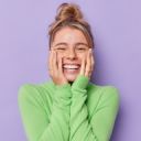 portrait-happy-young-female-model-keeps-hands-cheeks-smiles-broadly-shows-white-teeth-feels-glad-expresses-sincere-emotions-wears-green-turtleneck-isolated-purple-studio-background 1 Blonde mevrouw