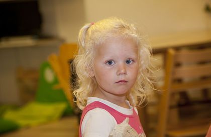 Meisje met blonde krullen kijkt in camera.