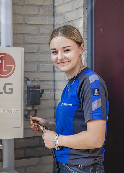 Hulpmonteur van DI Koeltechniek is bezig met het uitvoeren van taken en kijkt hierbij de camera in