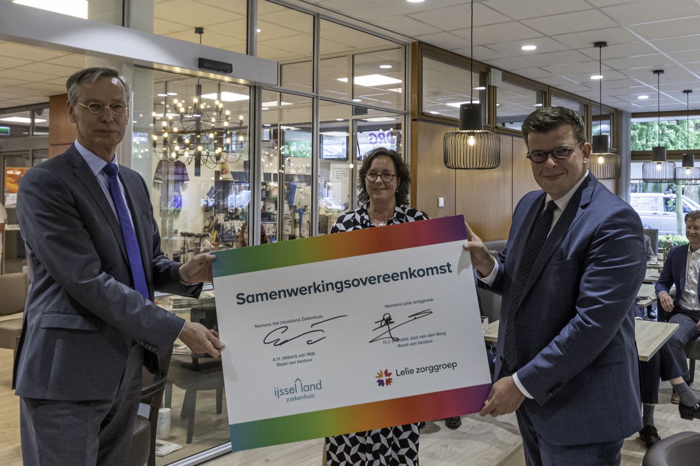 Opening polikliniek Kralingen Drie mensen houden samen een groot canvas omhoog waarop de samenwerkingsovereenkomst staat tussen Lelie zorggroep en het IJsselland Ziekenhuis
