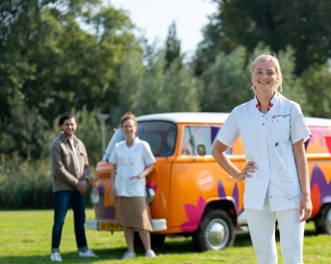 Medewerker in zorgjasje staat voor de oranje bus vol waardering en twee collega's van Lelie zorggroep