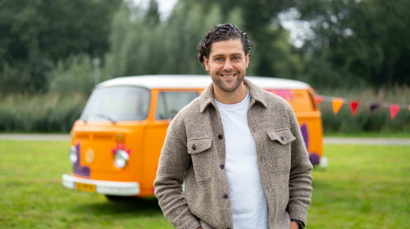 Bus vol waardering medewerker man vacature Lelie zorggroep campagne zonderuniform ondersteuning hulpverlening facilitair Man poseert glimlachend voor oranje vintage volkswagenbusje van Lelie zorggroep