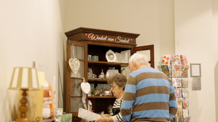 Echtpaar staat bij kast met spullen van Winkel van Sinkel Echtpaar staat bij kast met spullen van Winkel van Sinkel