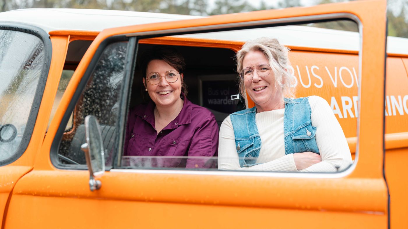 Werving vacature collega bus vol waardering portret Veluwe zorgjasje verpleeghuiszorg thuiszorg voor christelijke zorgorganisatie Lelie zorggroep Twee vrouwen staan en zitten in de bus vol waardering