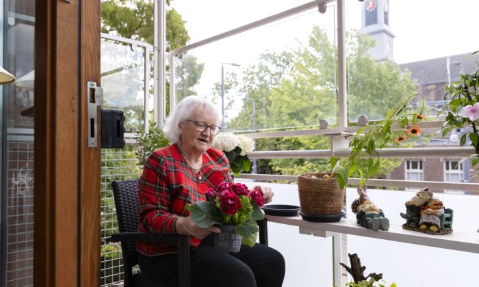 Bewoner balkon bloemen - web Client van verpleeghuis Pniel in Kralingen op balkon met bloemen met uitzicht op de Oudedijk