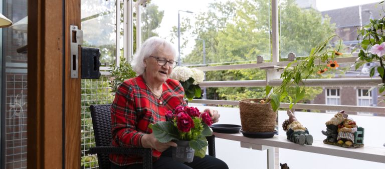 Bewoner balkon bloemen - web Client van verpleeghuis Pniel in Kralingen op balkon met bloemen met uitzicht op de Oudedijk
