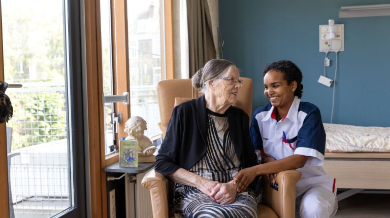 Bewoner en zorgverlener in stoel op eigen kamer Client en zorgverlener in uniform lachen samen in eigen kamer in verpleeghuis Pniel in Rotterdam Kralingen