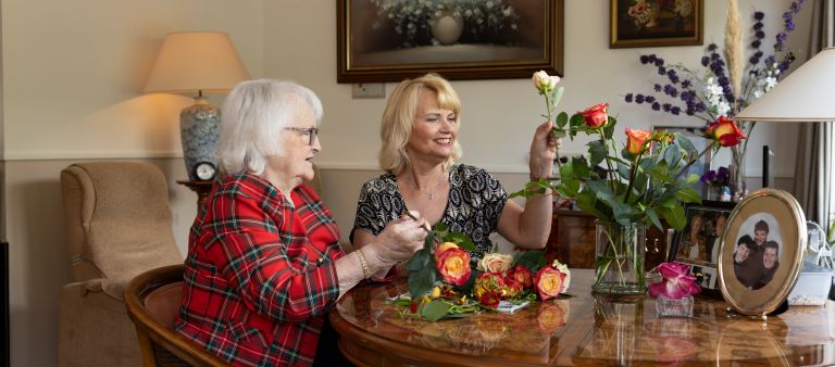 Bewoner mantelzorger bloemschikken appartement - web Oude vrouw en vrouwelijke begeleider zijn aan het bloemschikken aan tafel in huis