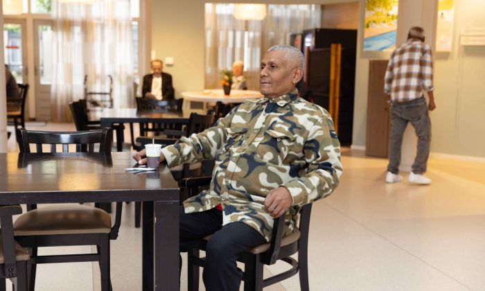 Bewoner zit in de ontmoetingsruimte van Korsakov Expertisecentrum Slingedael in Rotterdam en drinkt koffie Meneer in legerkleurig vest zit met een kopje koffie aan een tafel in de ontmoetingsruimte van Slingedael en staart apatisch voor zich uit