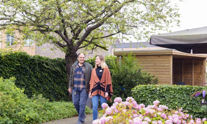 Bewoner en medewerker van Korsakov Expertisecentrum Slingedael lopen een rondje in de tuin vacature sph social work hulpverlening verpleeghuiszorg Oudere man en jongere vrouw lopen naast elkaar in de tuin van Slingedael en lachen naar elkaar