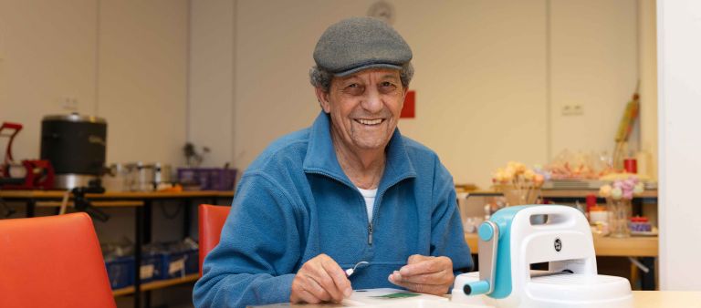 Bewoner werkt bij de werkplaats van Korsakov Expertisecentrum Slingedael in Rotterdam Meneer lacht terwijl hij aan de werktafel zit en bezig is met zijn zelfgemaakte klusproject