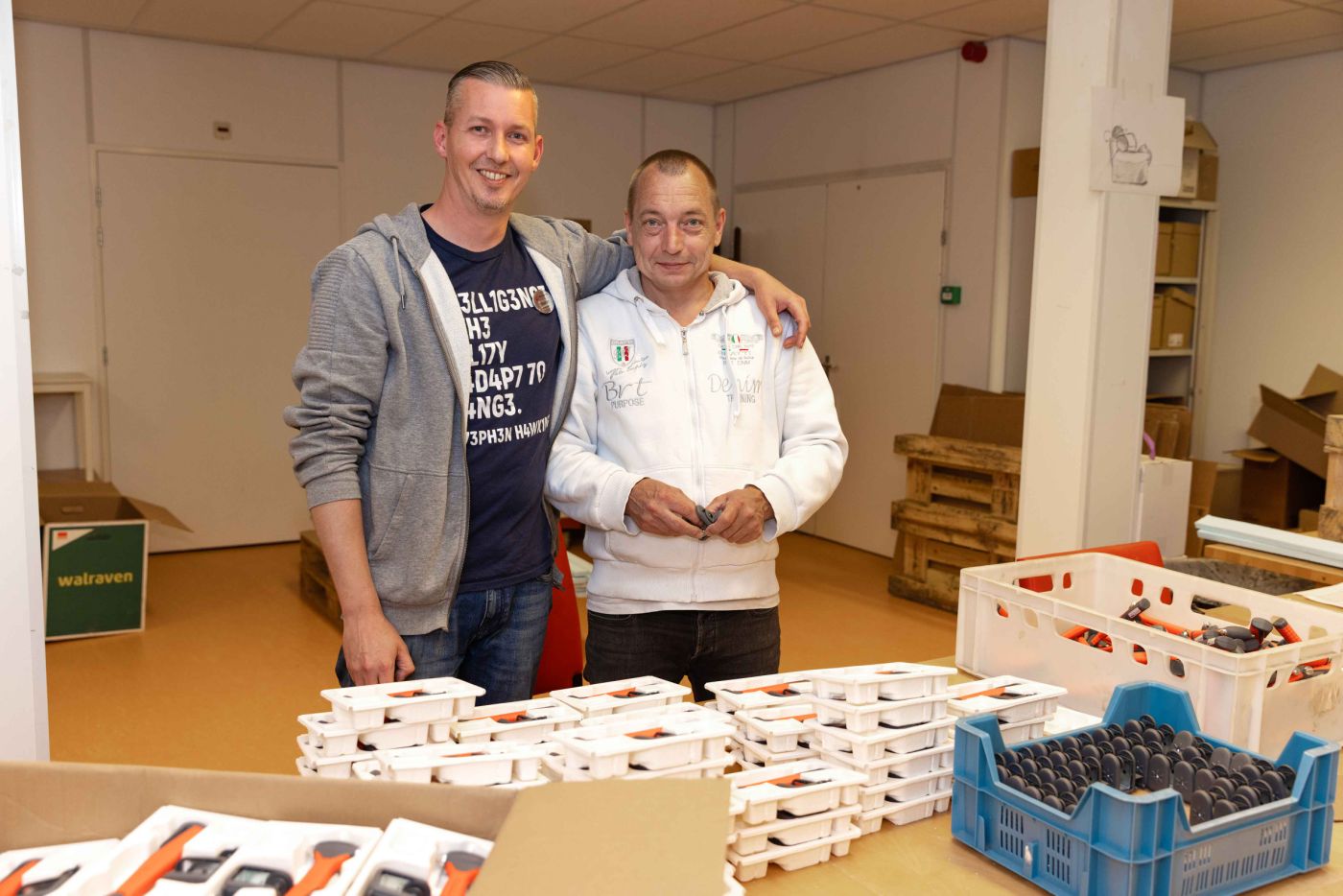 Bewoner werkt samen met medewerker bij de werkplaats van Korsakov Expertisecentrum Slingedael in Rotterdam welzijn vacature dagbesteding Twee mannen staan bij een werktafel in de werkplaats van Slingedael en de ene man heeft zijn arm om de schouder van de andere man geslagen