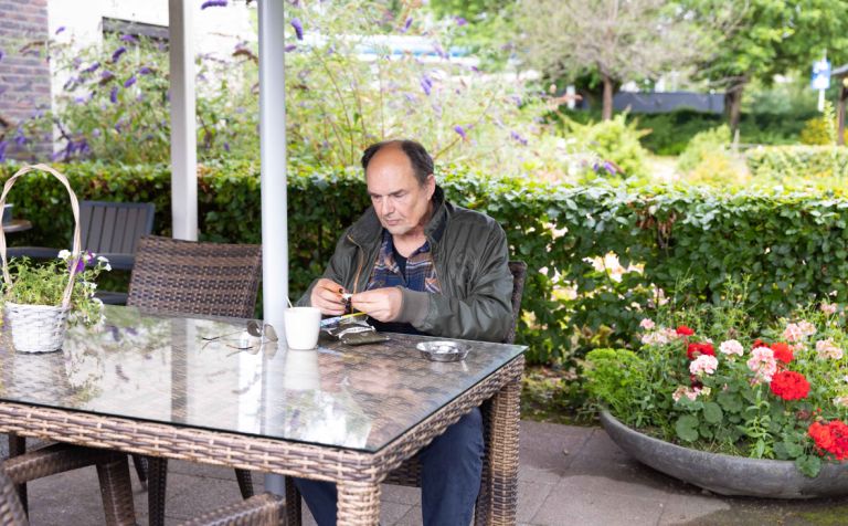 Bewoner met syndroom van Korsakov rolt een sigaret in de tuin van Korsakov Expertisecentrum Slingedael in Rotterdam Meneer zit aan een tuintafel in de tuin van Korsakov Expertisecentrum Slingedael en rolt een sigaret