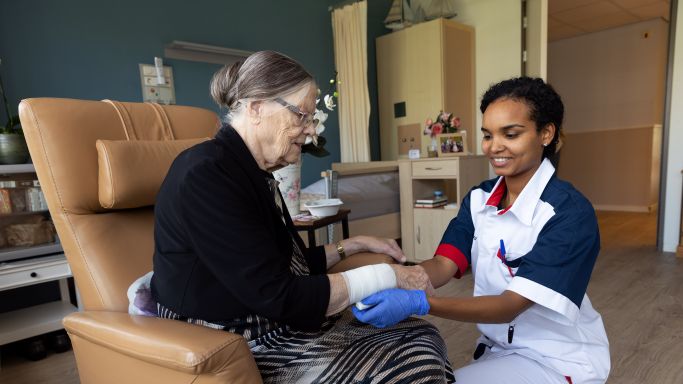 Client in christelijk verpleeghuis Pniel in Rotterdam Kralingen wordt verbonden door zorgmedewerker in zorgjasje Arm van een bewoner wordt verbonden door zorgverlener