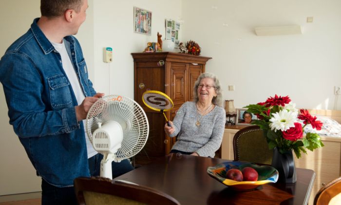 Bewegingsagoog en bewoner spelen spelletje in christelijk verpleeghuis De Burcht in Rotterdam Het Lage Land Jonge man en oude vrouw staan rond een ventilator en de vrouw slaat met een racket zeepbellen weg die de ventilator wegblaast.