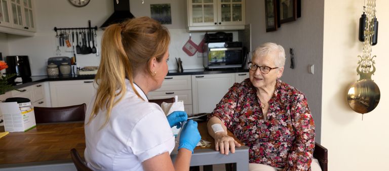 Cliënt arm op tafel zorgverlener verbinden in keuken Vrouwelijke verpleegkundige verzorgt wond op arm van oudere dame in huis