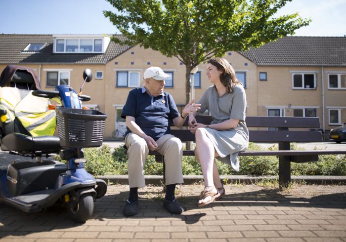 Cliënt dementie zittend op bankje buiten pratend met zorgverlener liggend beeld vacature hulpverlening casemanager dementie Zorgverlener en cliënt op bankje ervaren de visie en missie van Lelie zorggroep in de praktijk