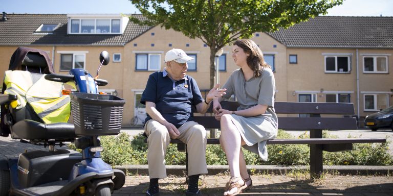 Cliënt dementie zittend op bankje buiten pratend met zorgverlener liggend beeld vacature hulpverlening casemanager dementie Zorgverlener en cliënt op bankje ervaren de visie en missie van Lelie zorggroep in de praktijk